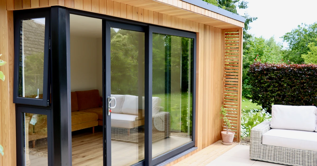 aluplast aero-slide black inline sliding door installed on a wooden garden room with outdoor patio furniture and greenery