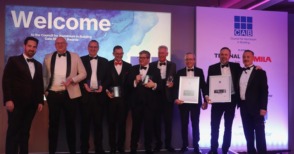 Nine men in black-tie attire standing on a stage with awards, 'Welcome to the Council for Aluminium in Building Gala Dinner & Awards' projected behind them