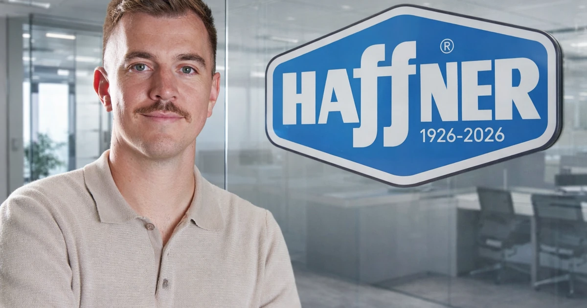 Man with short brown hair and moustache standing with arms crossed in front of glass office partition displaying Haffner logo