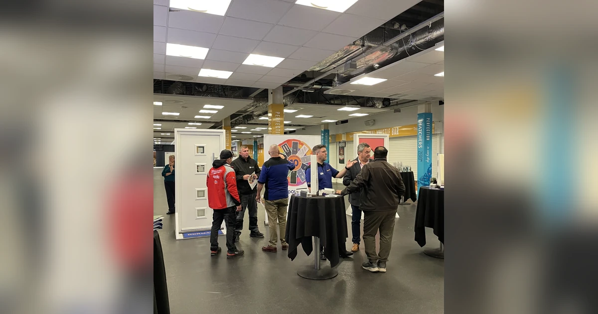 six people at a Hörmann Truedor event interacting around composite door displays and promotional materials in a large indoor venue