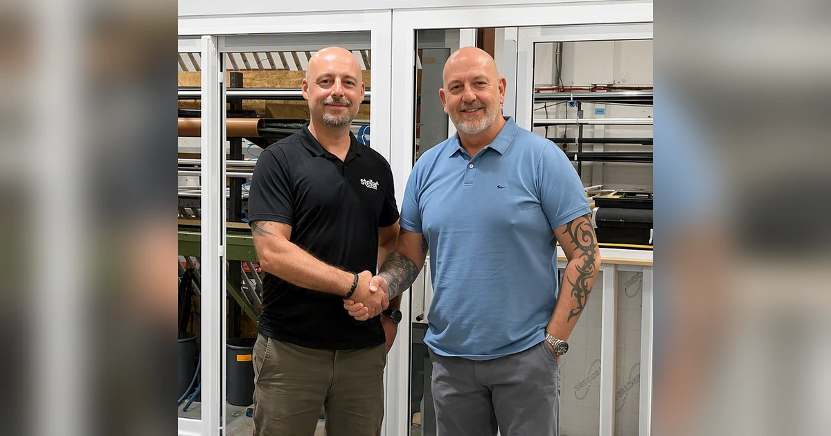Two men shaking hands in front of aluminium window frames and fabrication equipment in a workshop