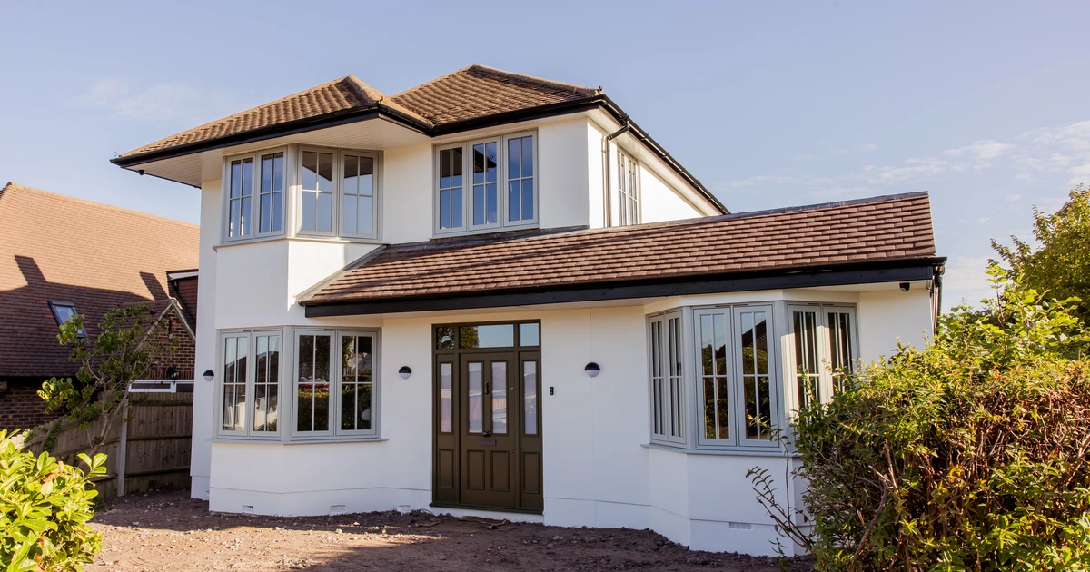 Renovated two-story house featuring Residence 7 windows and entrance door with a brown tiled roof and white walls under blue sky