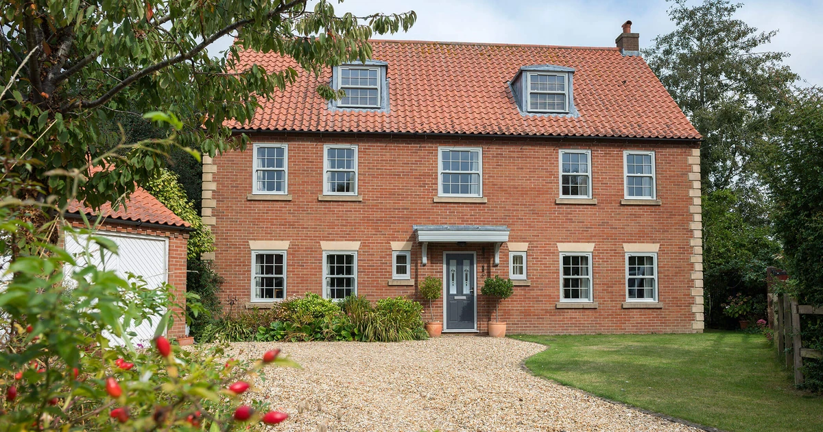Traditional brick house with multiple heritage-style sash windows and a tiled roof in a garden setting