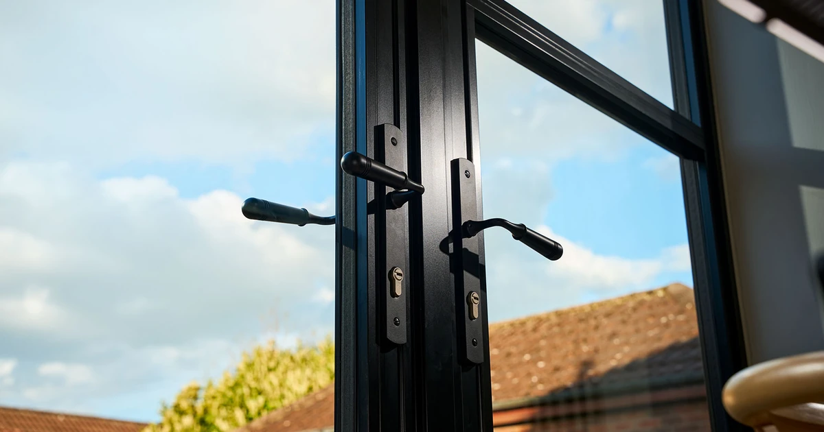 Close-up view of black heritage aluminium doors with slim dark frames, traditional handles, and glass panels showing an outdoor scene