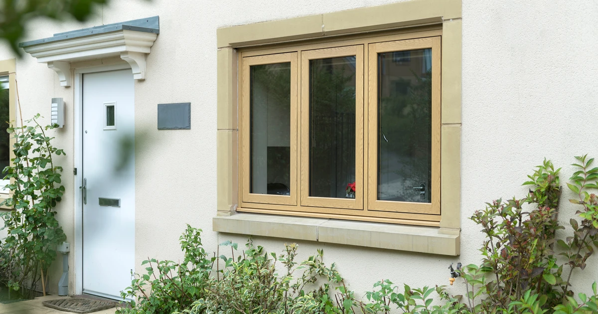 flush sash windows with woodgrain finish installed in a cream house with stone window frame and garden plants