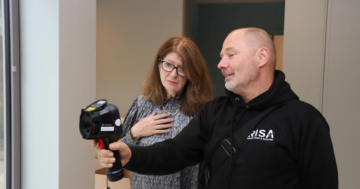 Two people indoors inspecting with a thermal imaging camera, one wearing glasses and the other a RISA logo hoodie
