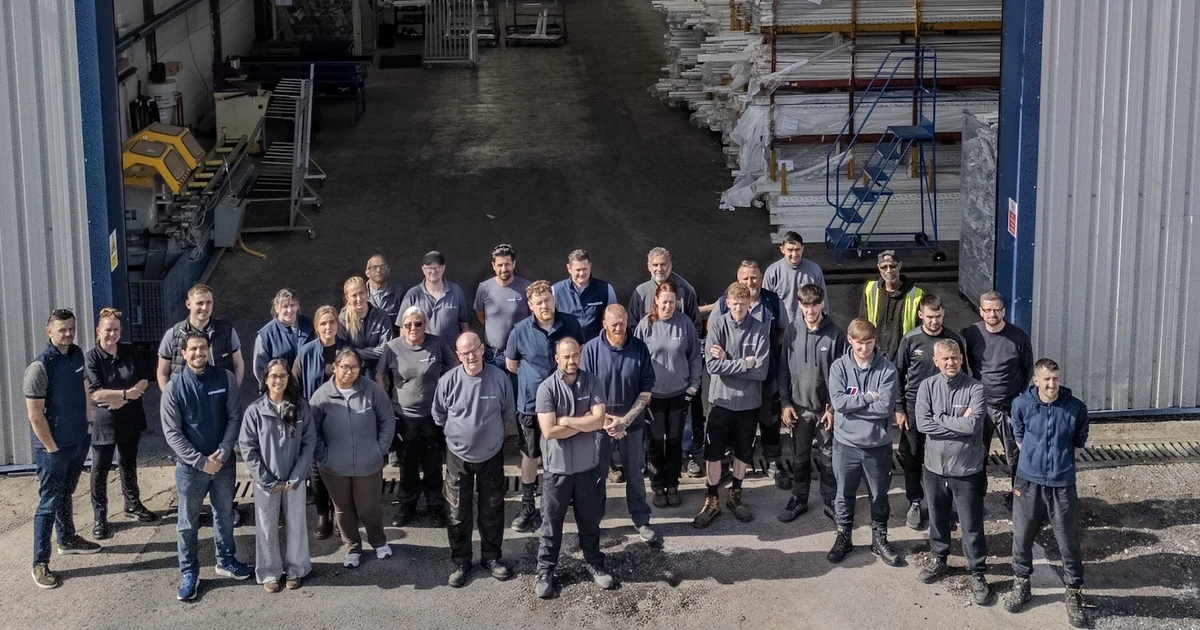Group of 35 AluFold Windows employees standing outside the factory at Whitebirk Industrial Estate under the company sign