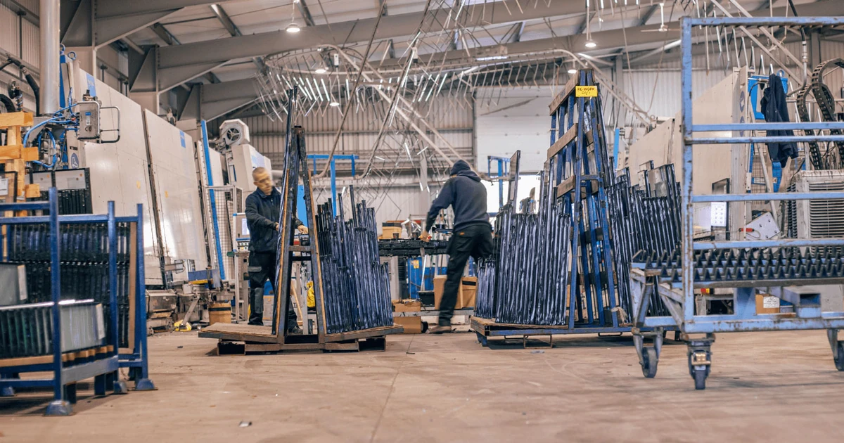 Two workers among racks of framed glass units on the factory floor at Clayton Glass Nottingham site