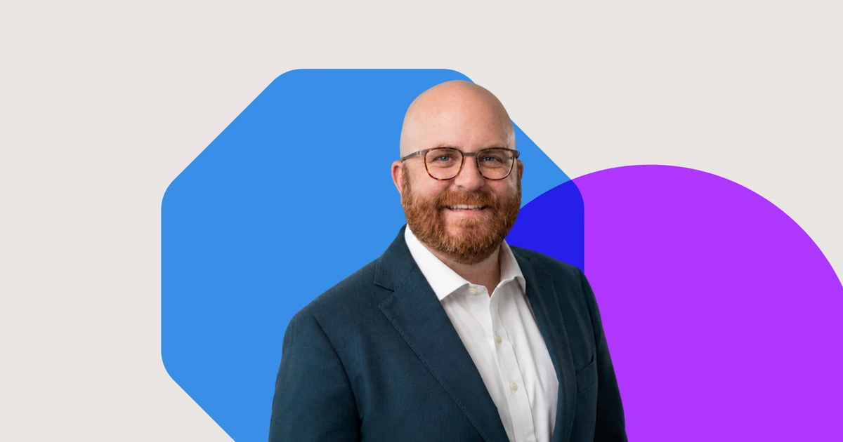 Steve Warfield wearing glasses, a white shirt and dark suit jacket, smiling against a light background with blue and purple shapes