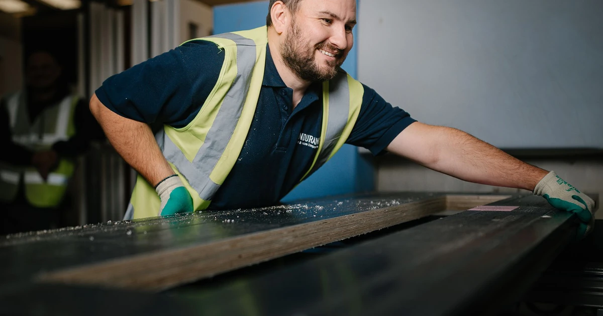 Smiling man in a high-visibility vest working on a large door frame in an industrial setting