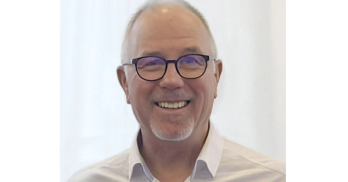 David Cahill — smiling man with glasses wearing a white shirt on a light blurred background