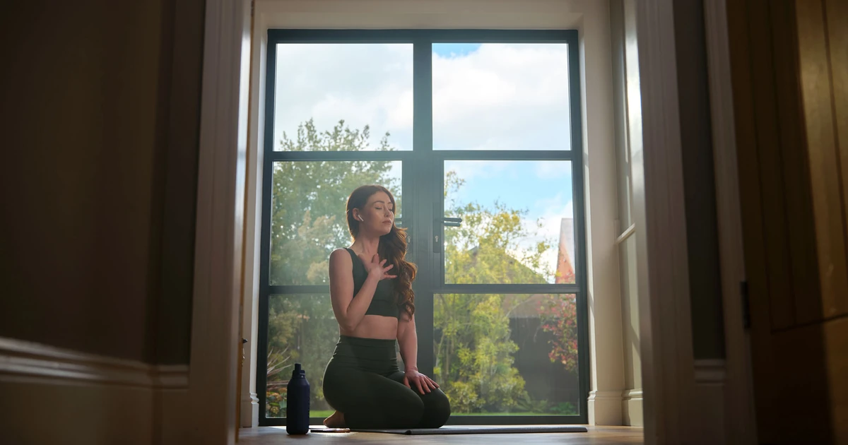 Woman doing yoga inside a home beside a large aluminium-framed window showcasing natural light and garden view