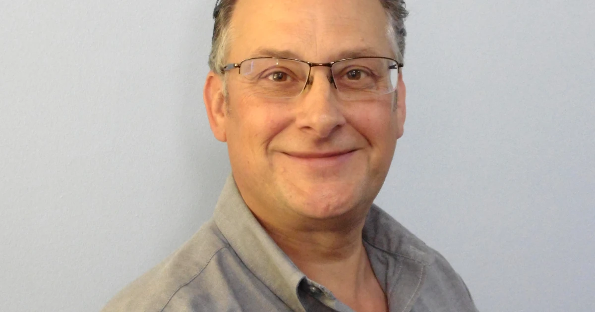 Mark Wilcox in a grey shirt smiling against a plain background