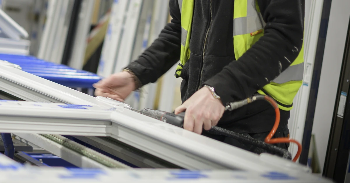 Two installers in high-visibility vests working on window frames in a workshop setting
