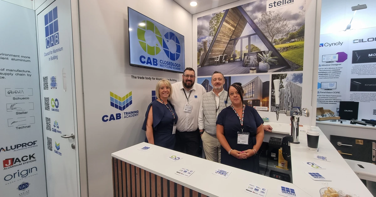 Four people standing inside a CAB exhibition booth with branding and aluminium product displays in the background