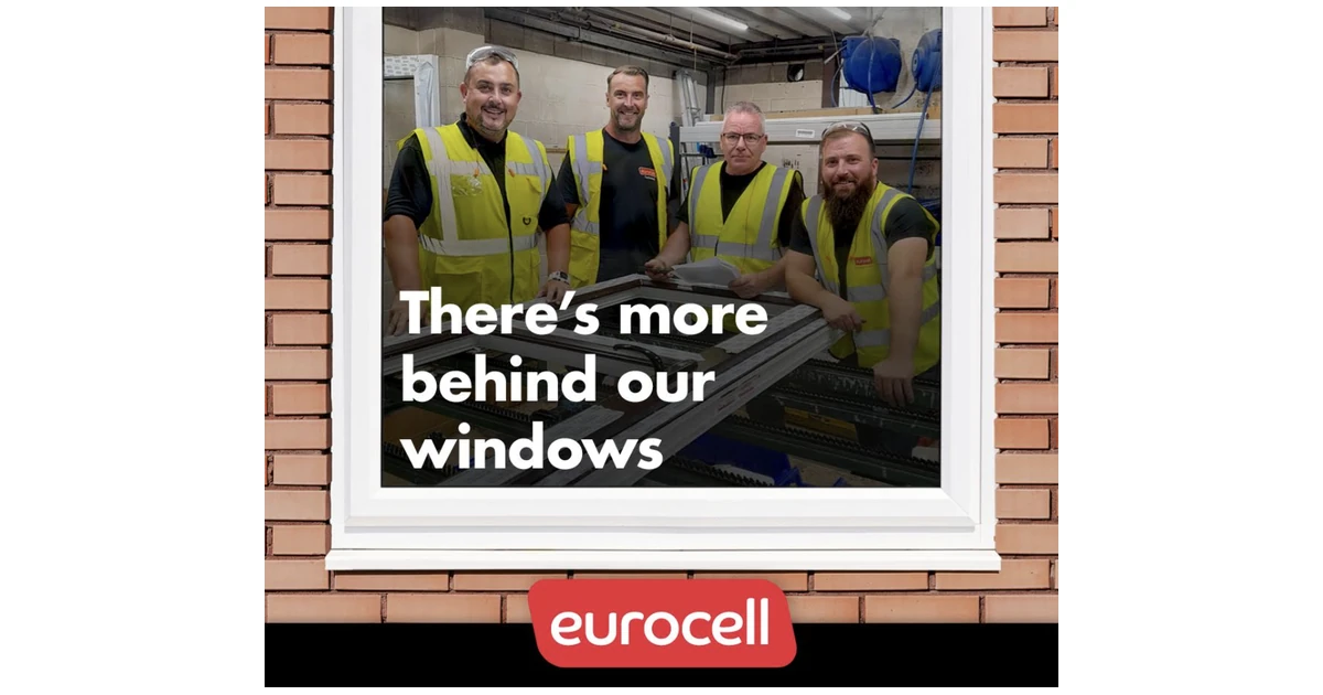 Four workers wearing high-visibility vests standing behind a window frame inside an industrial facility
