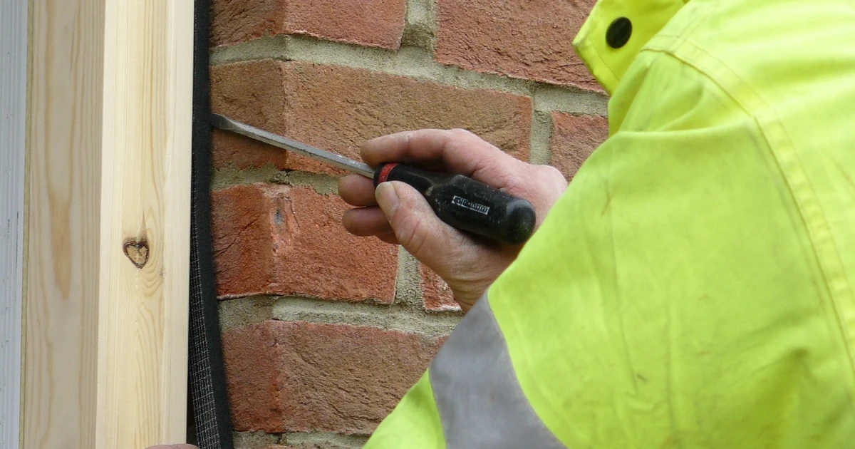 Person in hi-vis jacket installing foam tape around window frame on brick wall