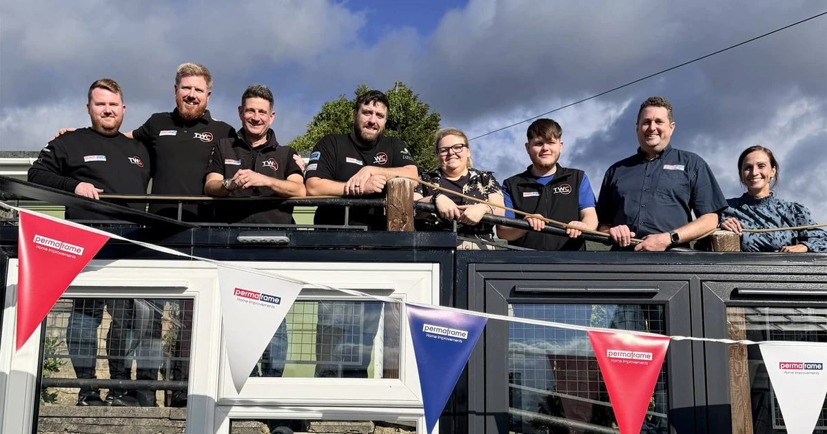 Eight Permaframe and TWC employees standing behind a railing decorated with Permaframe bunting under a cloudy sky.