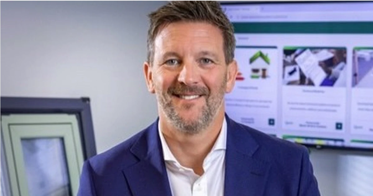 Professional man in blue suit sitting indoors with windows and display screens in the background