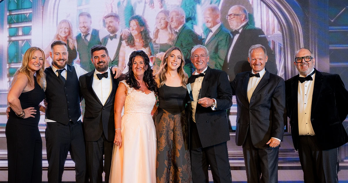Group of nine people dressed formally standing on stage holding an award at the Oldham Business Awards