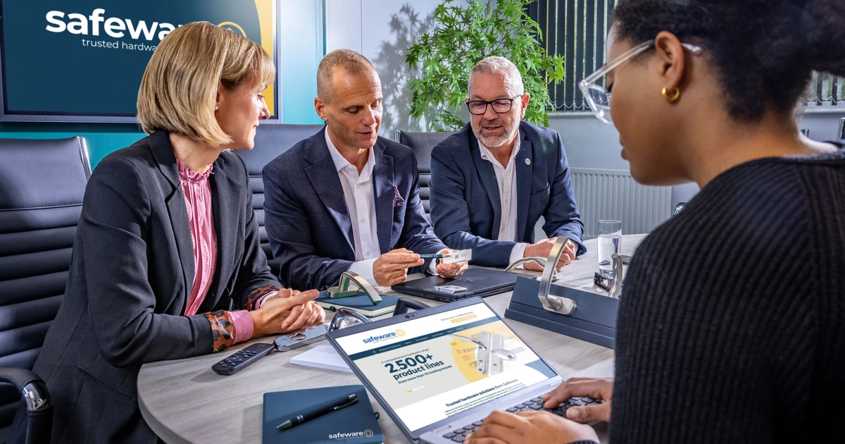 Four professionals in meeting room around table discussing hardware products with Safeware logo on screen
