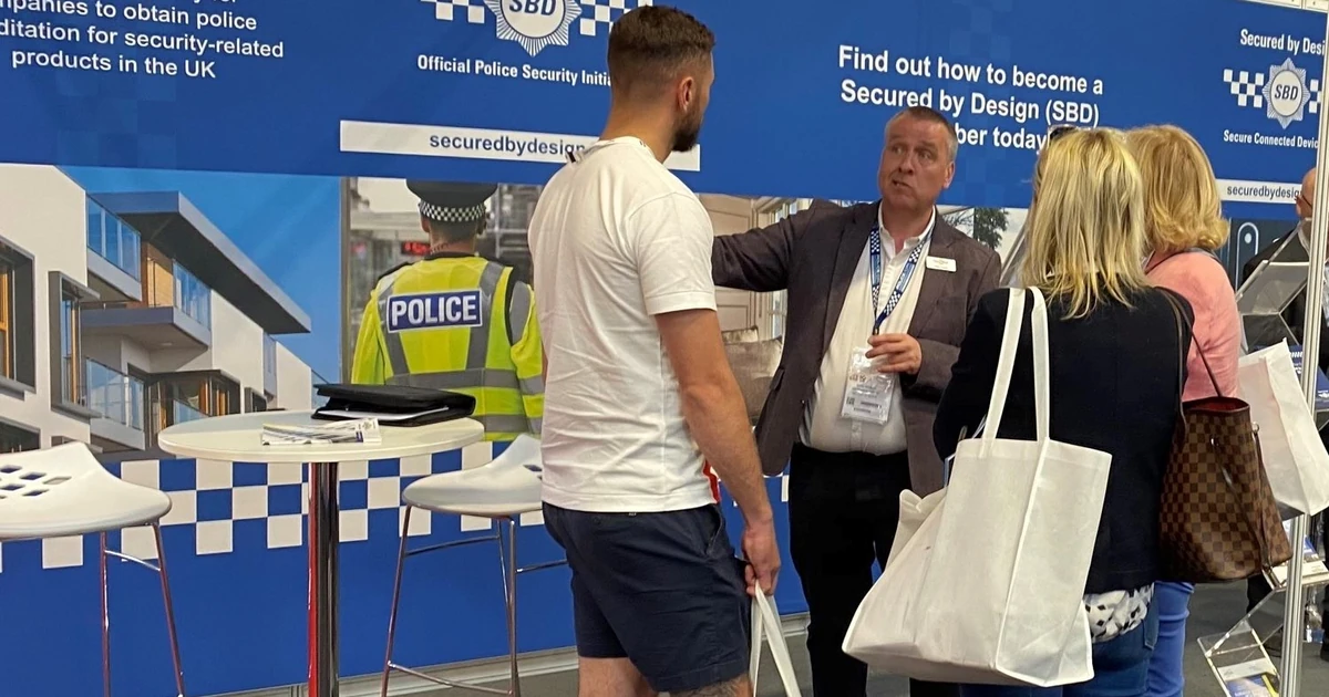 Group of four people engaged in discussion at the Secured by Design exhibition booth at a trade show