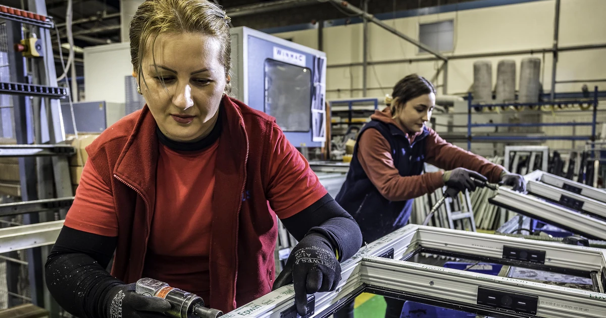 Two factory workers assembling window frames in an industrial setting